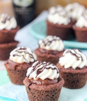 Four mouthwatering chocolate cookie cups on a teal napkin, the cookies are drizzled with whipped cream and chocolate