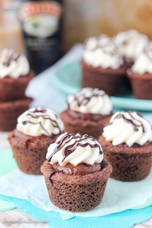 Four mouthwatering chocolate cookie cups on a teal napkin, the cookies are drizzled with whipped cream and chocolate