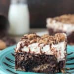 A slice of chocolate chip cookie poke cake, a chocolate cake with a chocolate chip cookie crust, chocolate pudding filling, and topped with a chocolate chip cookie mousse.