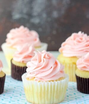 A few yellow cupcakes in liners and topped with a pink frosting.