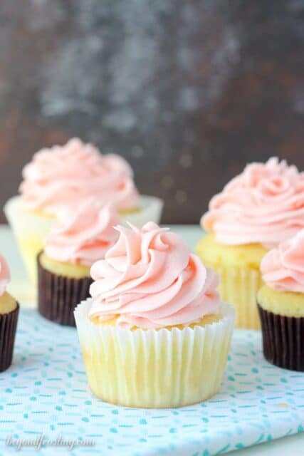 A few yellow cupcakes in liners and topped with a pink frosting.