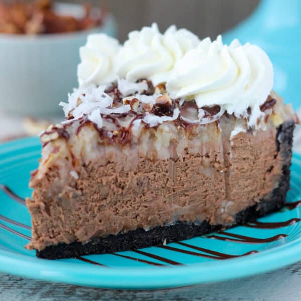 A slice of German chocolate cheesecake topped with coconut and whipped cream on a blue plate.