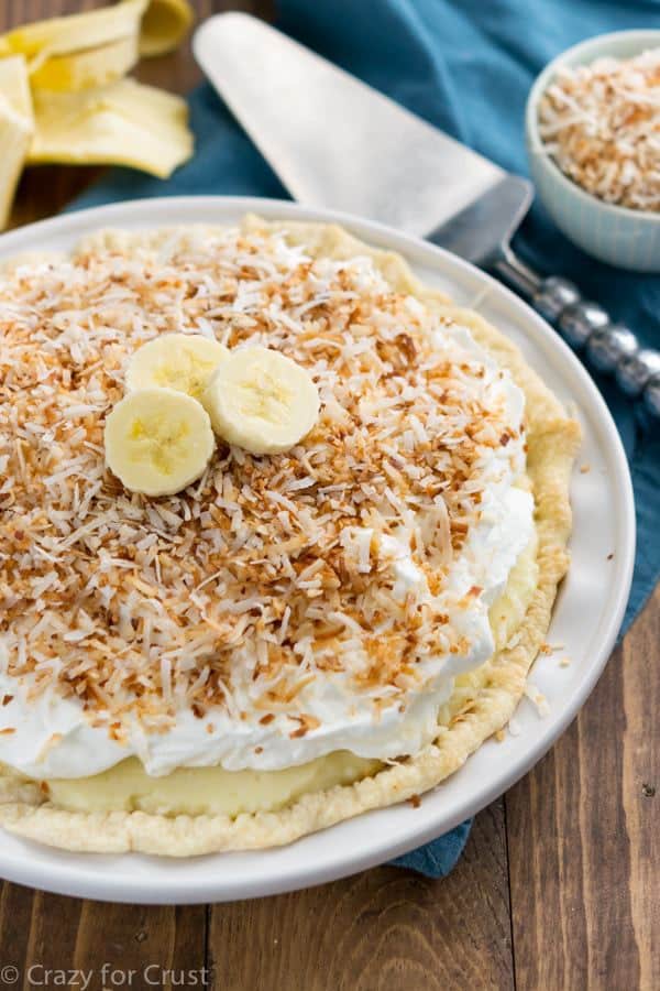 A Coconut Banana Cream Pie on a White Serving Dish on Top of a Wooden Table