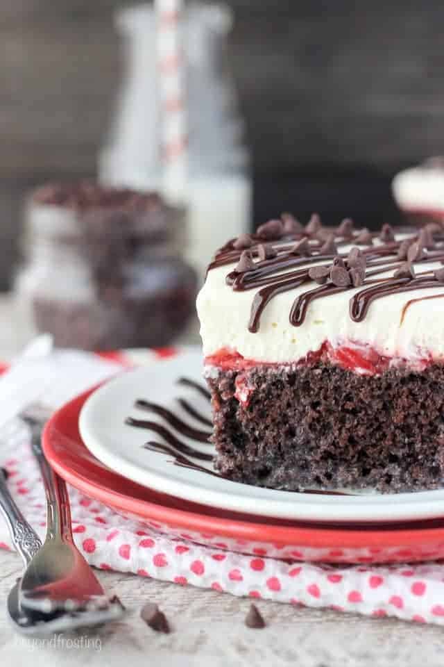 A piece of Chocolate Poke Cake with cherry filling and whipped cream on a white and red plate 