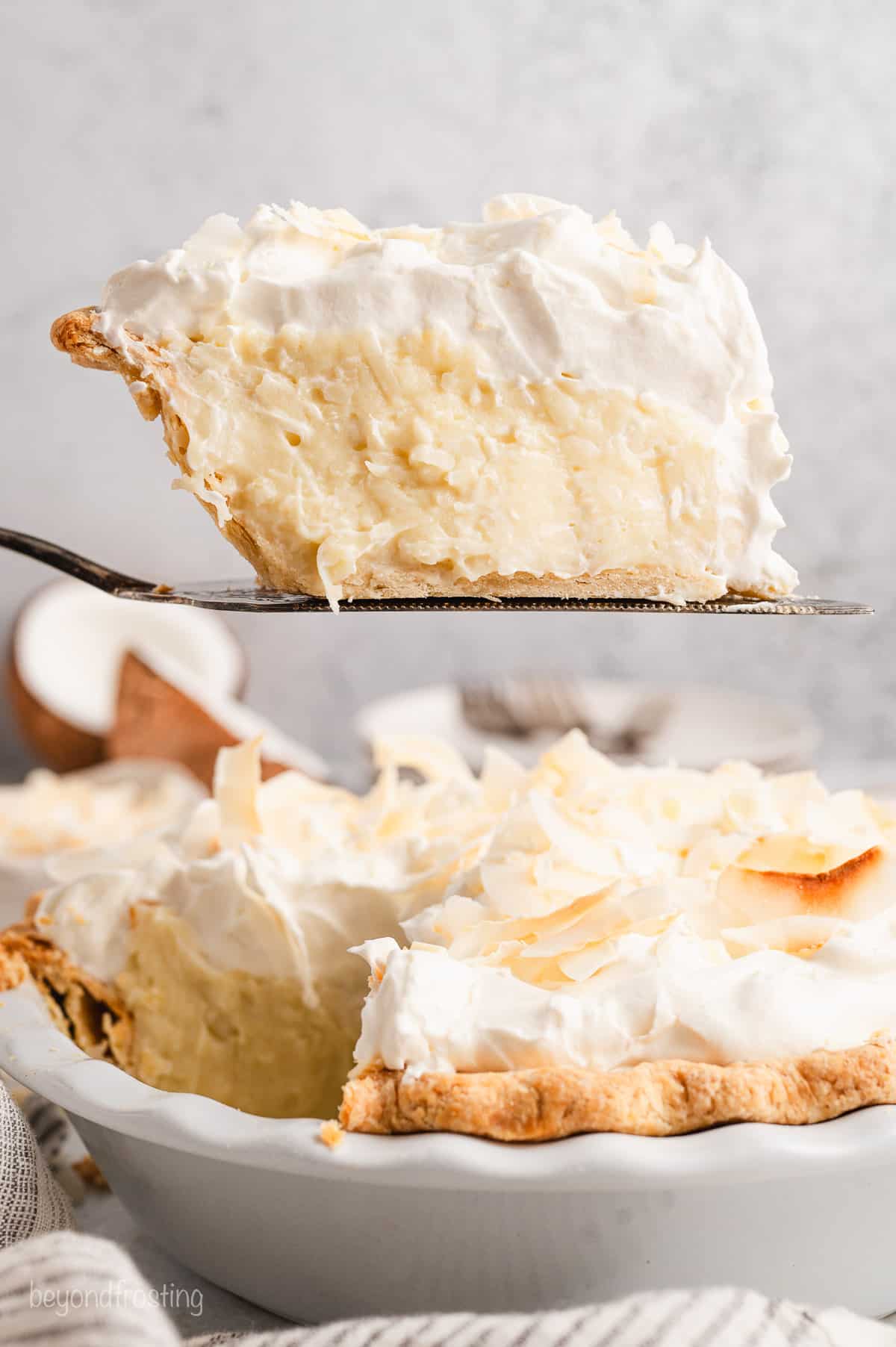 A slice of coconut cream pie being lifted from a pie plate.