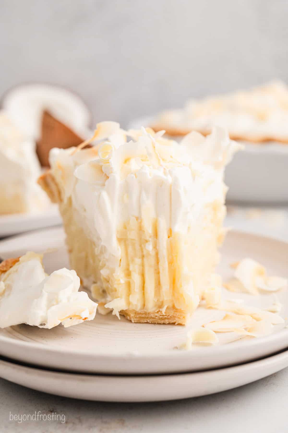 Close up of a slice of coconut cream pie on a plate, with a forkful missing from the end.