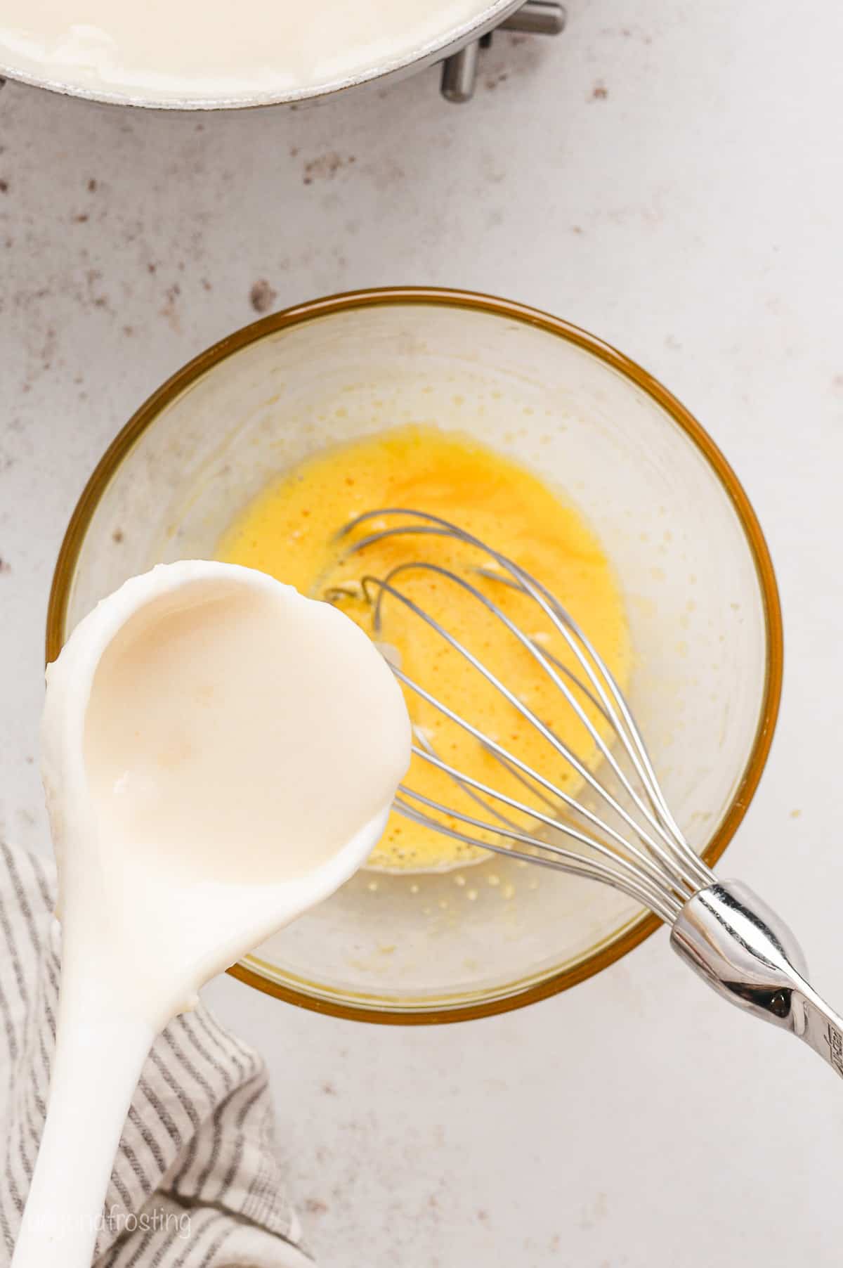 A half cup of filling mixture is poured over a whisk resting in a bowl of beaten eggs.