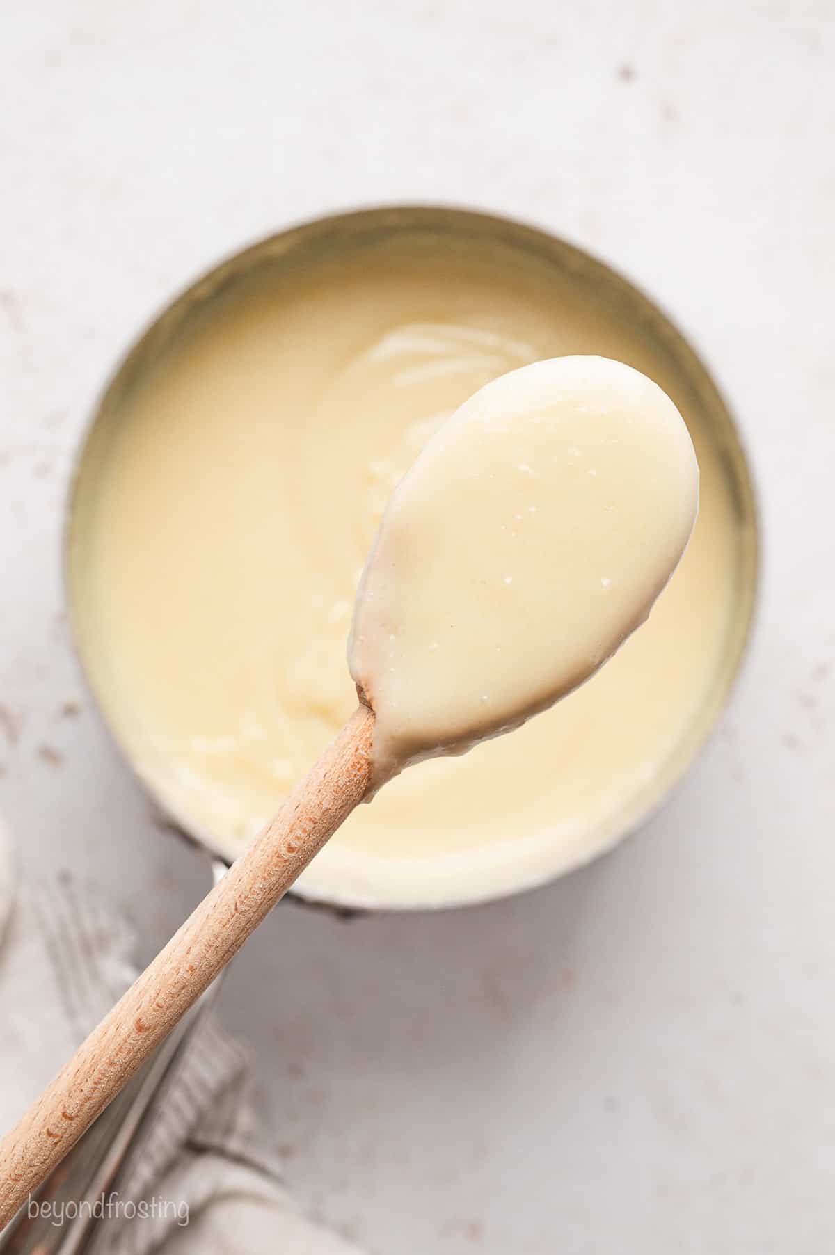A wooden spoon covered in coconut custard held over custard in a bowl.