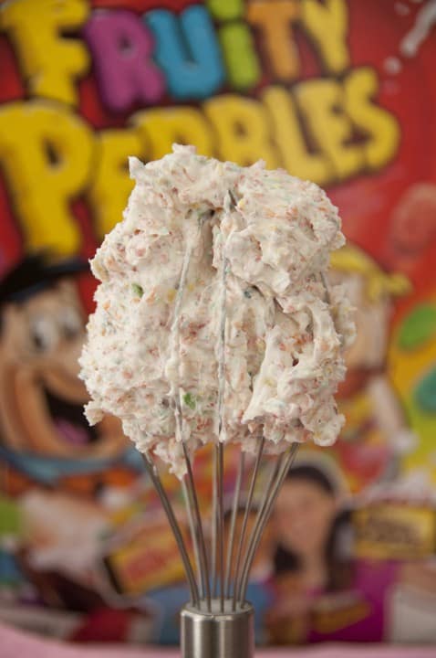 Fruity Pebbles Buttercream Frosting on a Whisk In Front of the Cereal Box