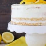 A Lemon Olive Oil Cake on a white cake stand with lemons on top