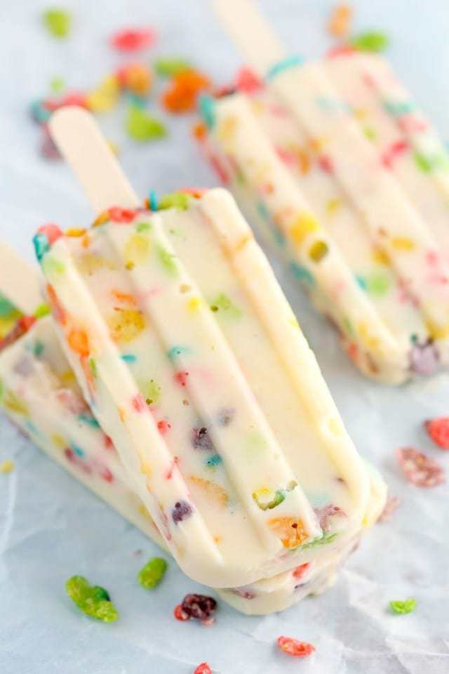 Three Marshmallow Fruity Pebbles Pudding Pops on Top of a Piece of Parchment Paper
