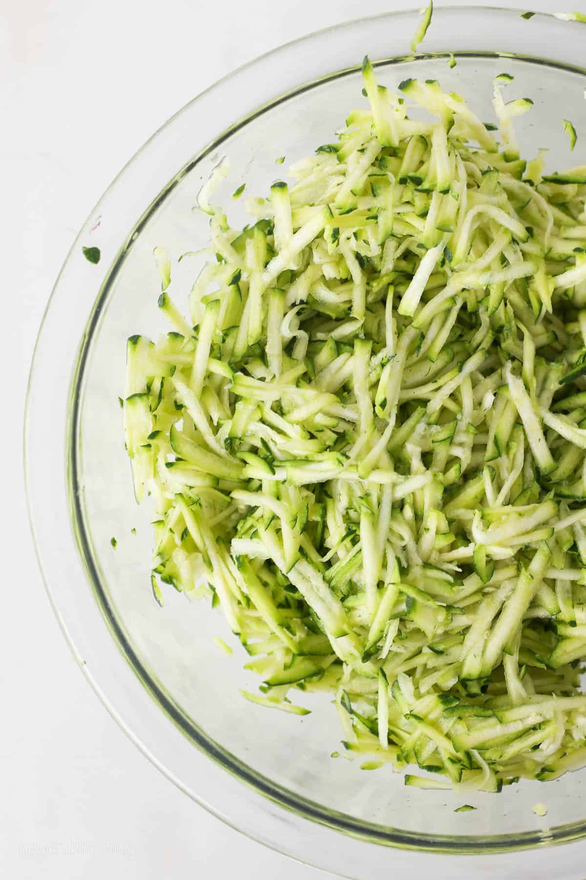 Overhead view of shredded zucchini in a glass bowl.