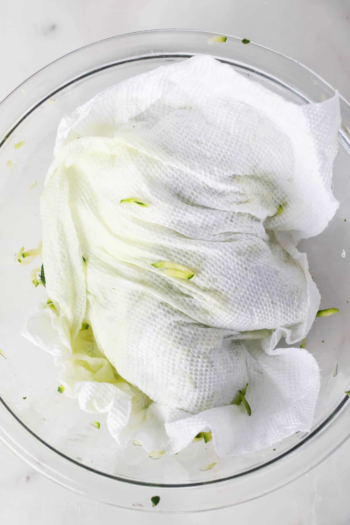 Paper towels pressed over a bowl of shredded zucchini.
