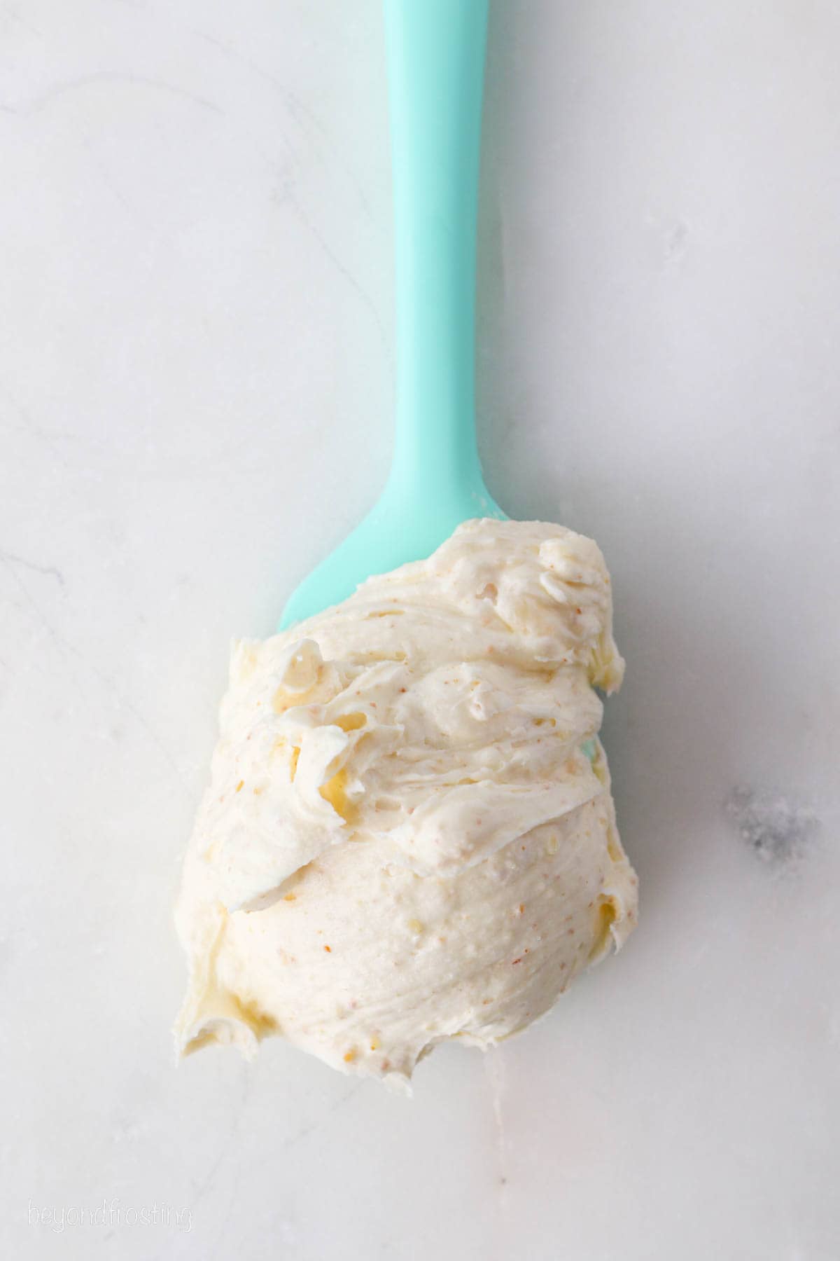 Brown butter frosting at the end of a blue spatula resting on a marble countertop.