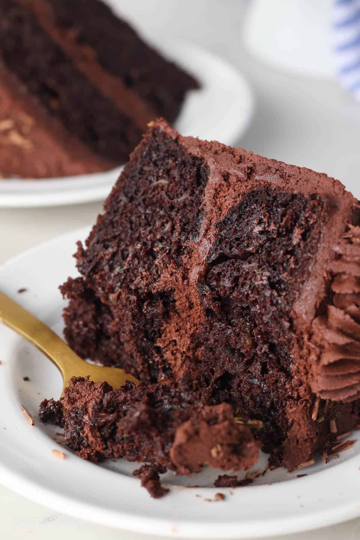 A forkful of frosted chocolate zucchini cake next to a slice of cake on a plate.