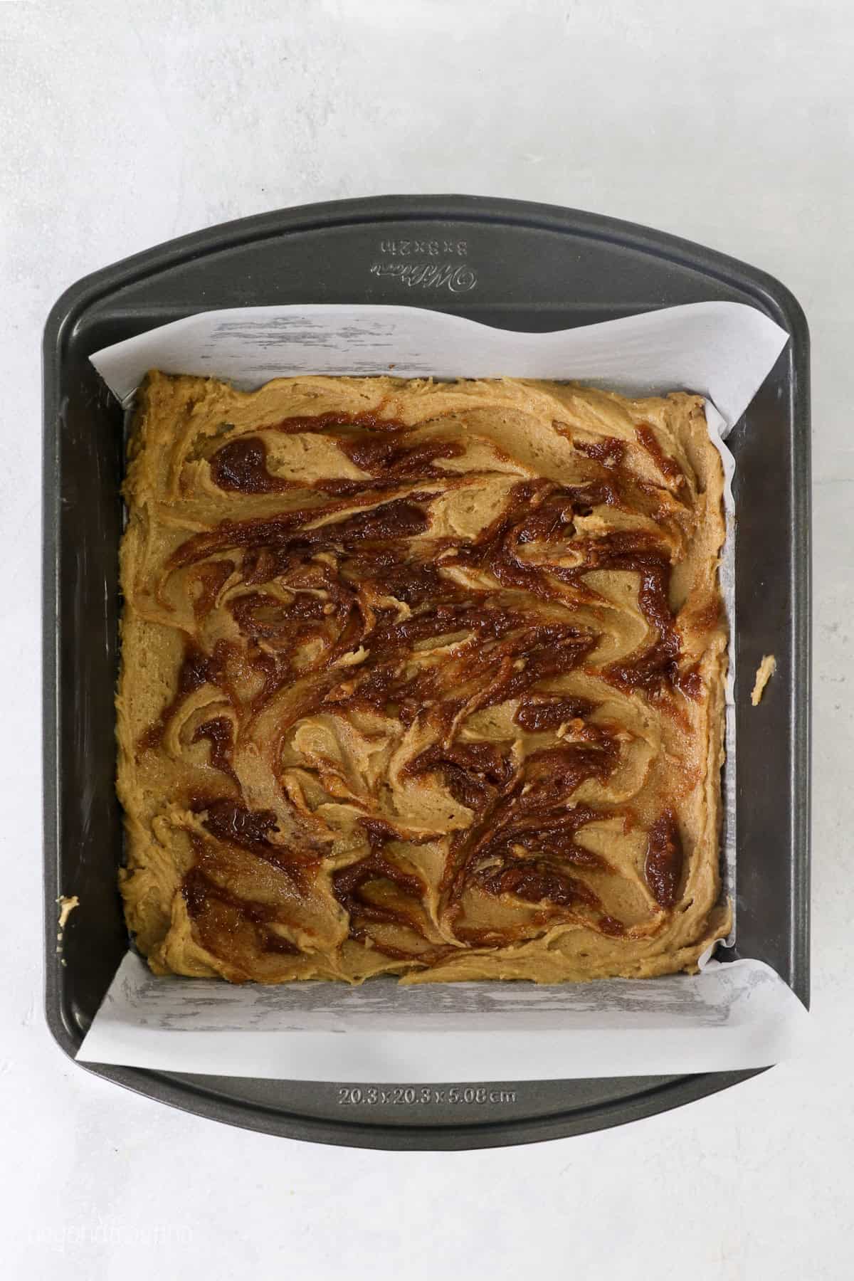 Blondie batter swirled with cinnamon sugar in a lined baking pan.