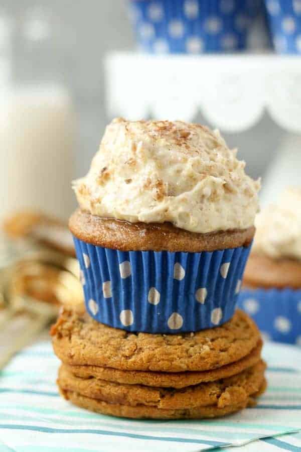 A cinnamon and brown sugar cupcake with a blue polka dot wrapper sitting on top of two oatmeal cream pies. The cupcake is topped with a big scoop of oatmeal cream pie frosting and dusted with cinnamon