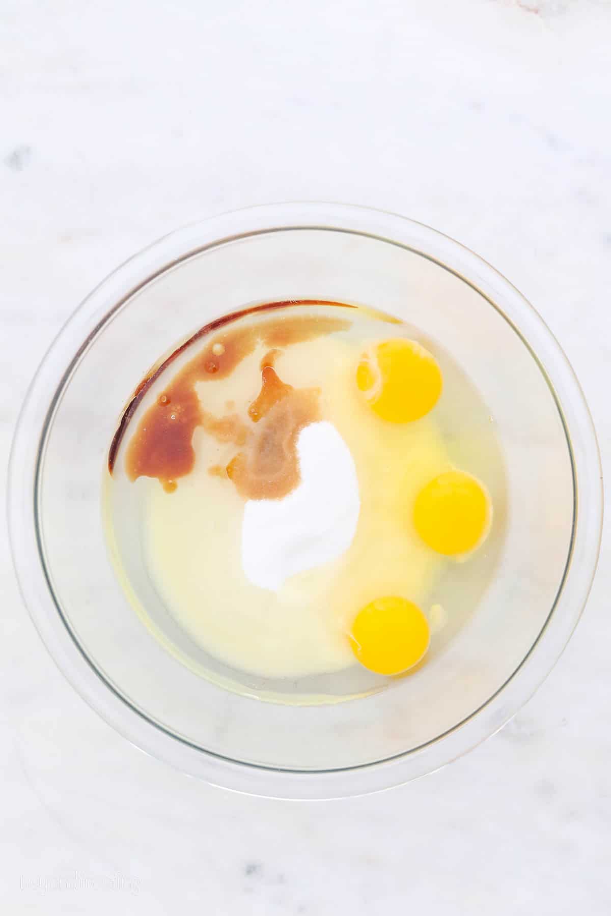 Eggs combined with the other wet ingredients for vanilla cake batter in a glass mixing bowl.