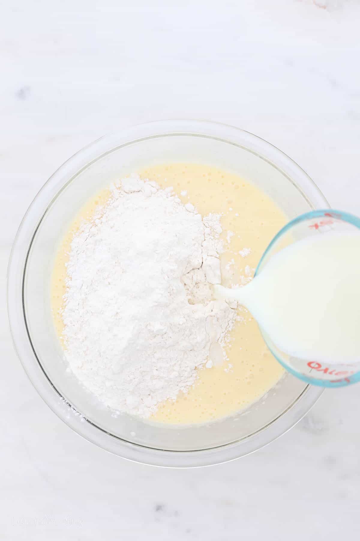 Milk is added to the cake batter ingredients in a glass mixing bowl.