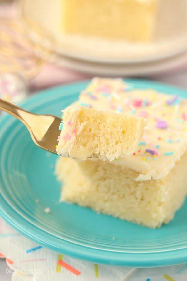 A gold fork holding a slice of vanilla cake. You can see the cake is blurred out in the background.