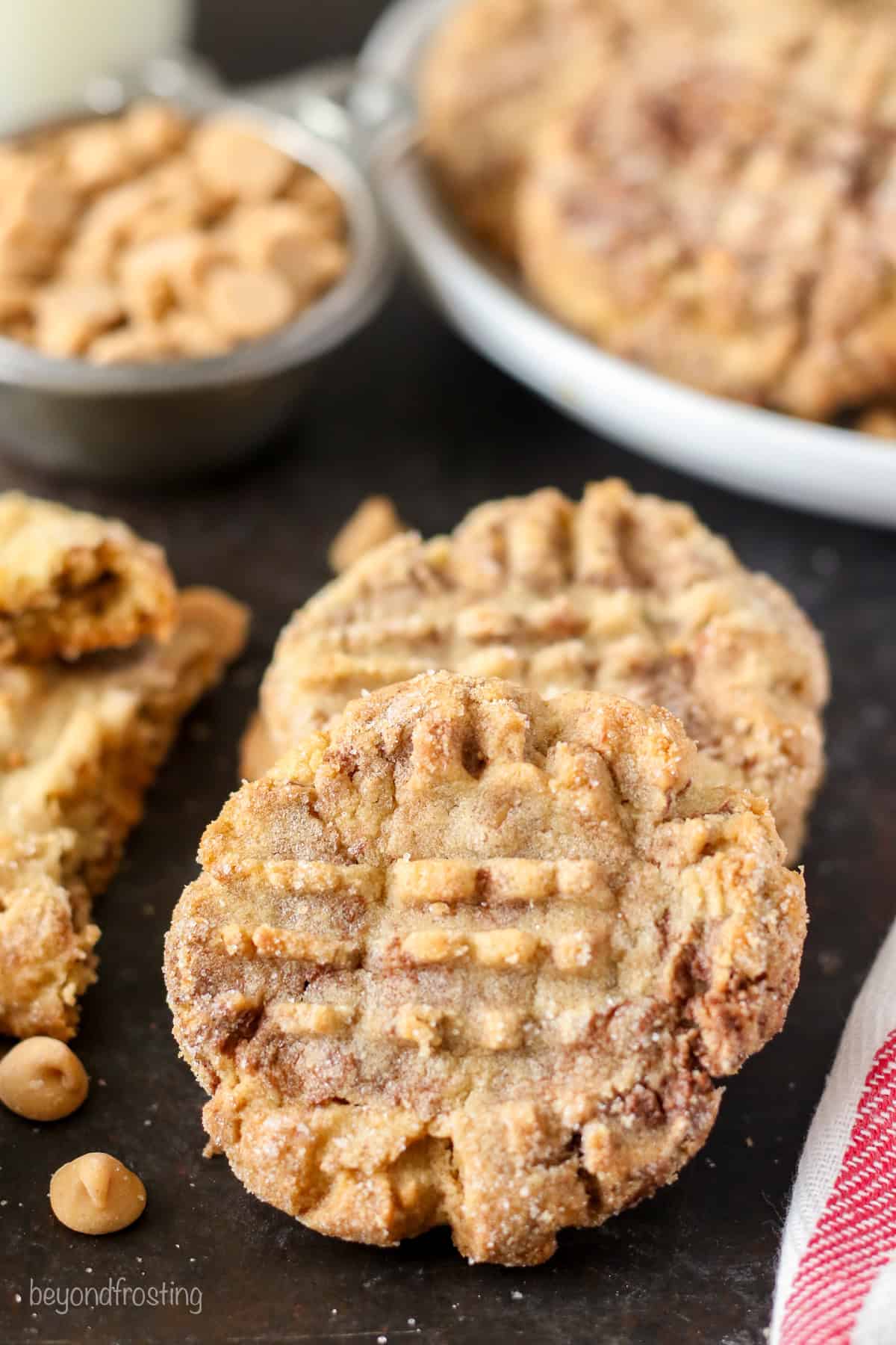 These peanut butter Nutella cookies are thick and chewy, soft-baked PB cookies swirled with fudgy Nutella and loaded with peanut butter chips! Close up of two peanut butter Nutella cookies with a plate of cookies in the background.