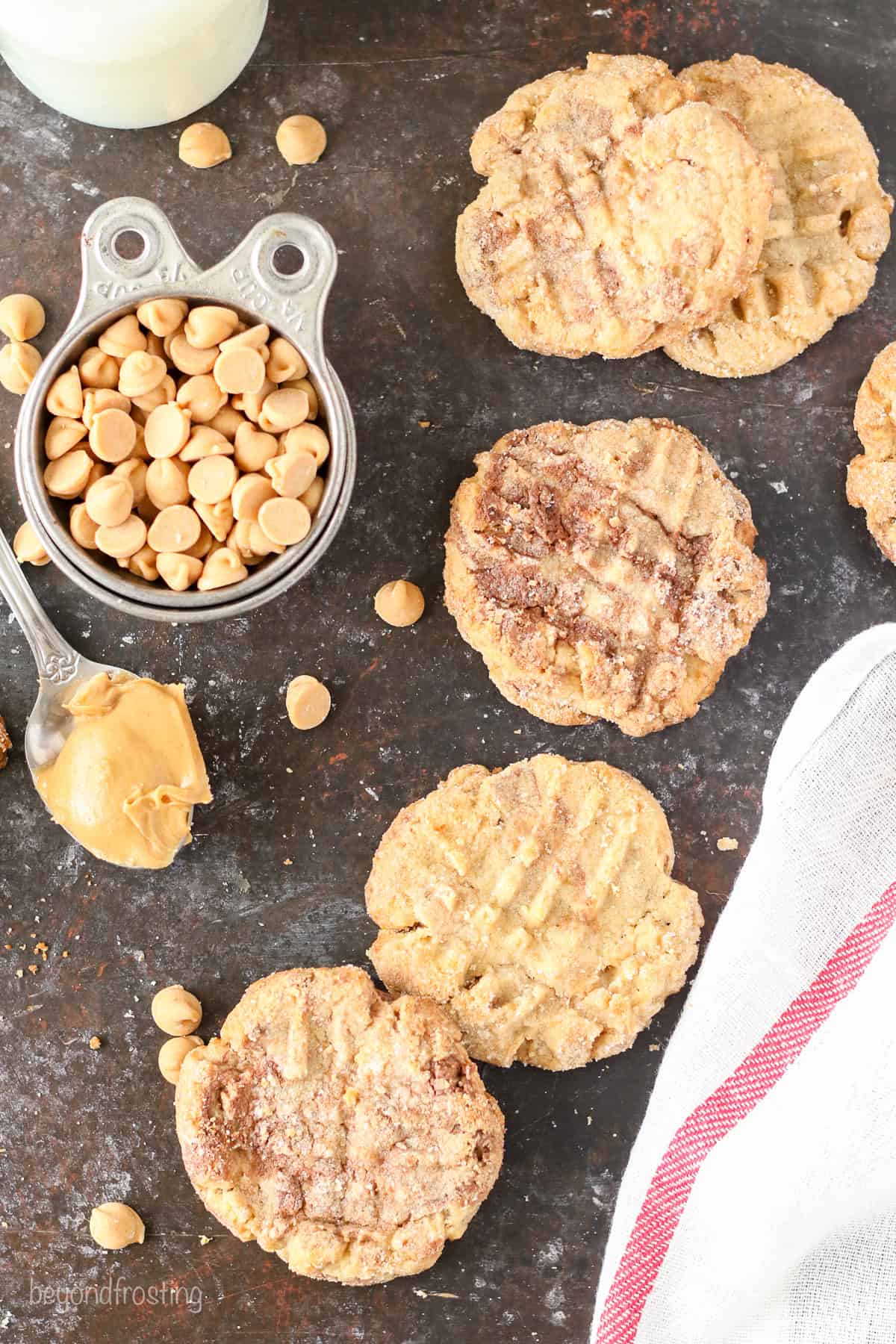 Overhead view of peanut butter Nutella cookies scattered over a countertop next to peanuts in a measuring cup.