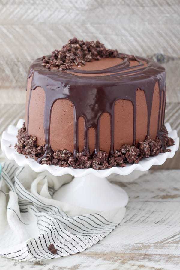 A gorgeous chocolate cake on a white rimmed cake stand with a chocolate ganache glaze