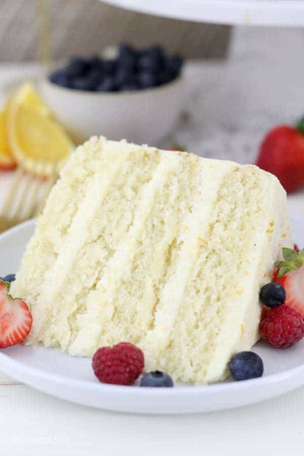 A close up shot of a 4 layer slice of cake with berries on the plate