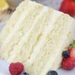 A close up shot of a 4 layer slice of cake with berries on the plate