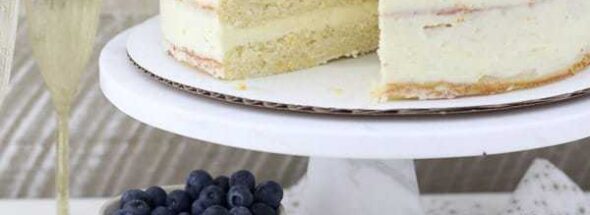 A Slice of Mimosa Cake with Fresh Berries Beside the Full Cake on a Cake Stand