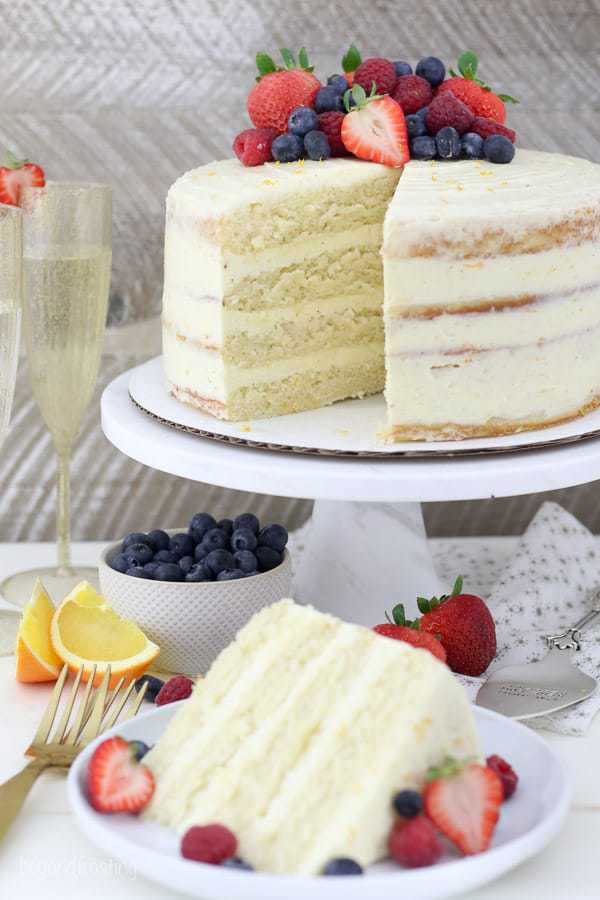 A gorgeous 4 layer cake with an assortment of berries on top, there's a slice missing showing the inside of the cake