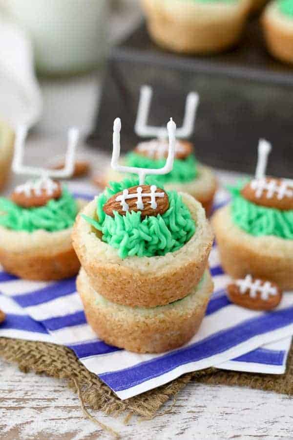 cookie cups filled with green frosting that looks like grass with a football shaped almond and a candy field goal