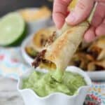 Dipping a half eaten taquitos into a bowl of green sauce