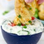 a soft pretzel being dipped into a cheese dip