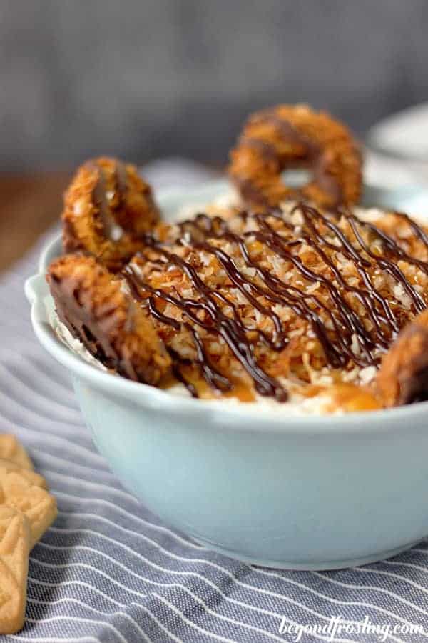A large bowl with a cheesecake dip topped with fudge and caramel and samoa cookies