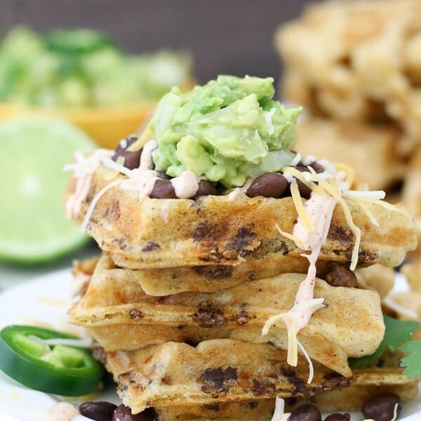 A plate of taco stuffed waffles with guacmole and beans on top