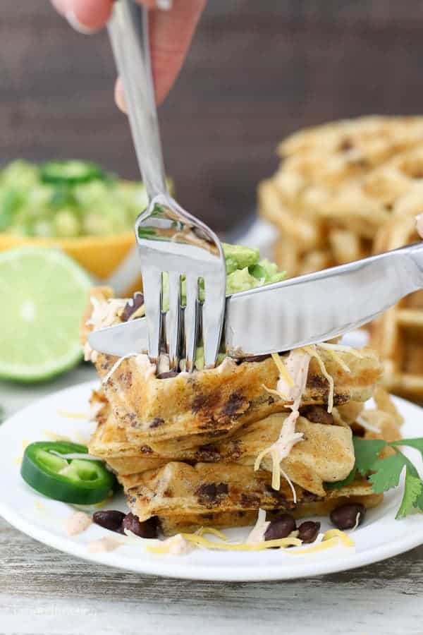 A fork and knife cutting through a plate of savory waffles