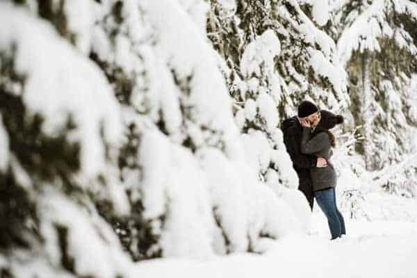 An engaged couple kissing in the snowy woods