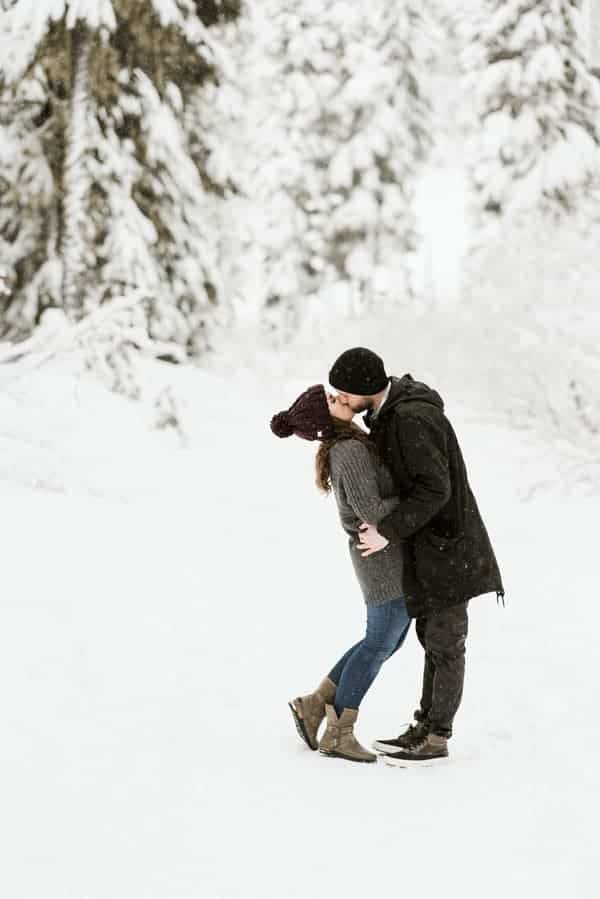 a couple kissing in the snowy wooded area