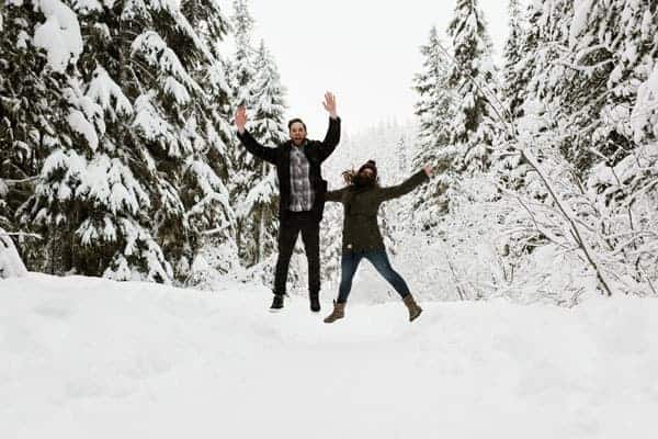 a couple jumps in the air in a snowy scenery