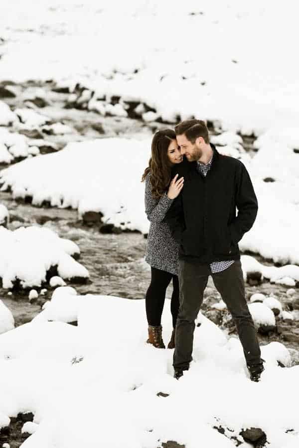 a couple standing on a rock in the middle of a snowy river