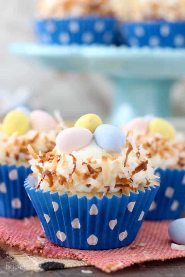 Easter themed Meyer Lemon cupcakes that look like a bird nest with chocolate eggs in the middle sitting on a teal cake plate.
