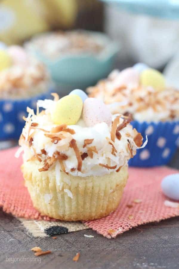 A lemon cupcake with a coconut frosting and toasted coconut with 3 easter eggs in the middle.