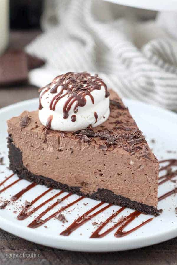 A slice of No-Bake Baileys Cheesecake on a white plate drizzled with chocolate.