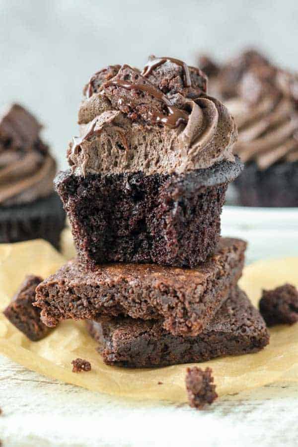 A brownie cupcake with a bite taken out of it sitting on top of two homemade brownies
