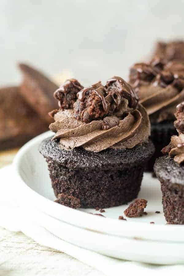 A triple chocolate brownie cupcake on a plate with more cupcakes and brownies in the background