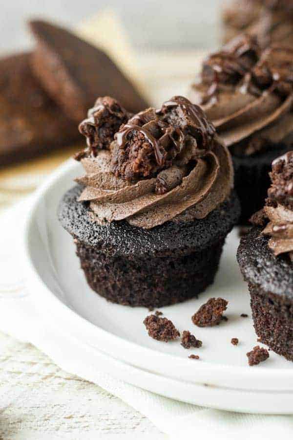 A chocolate cupcake on a white cake plate topped with brownie frosting and brownie chunks