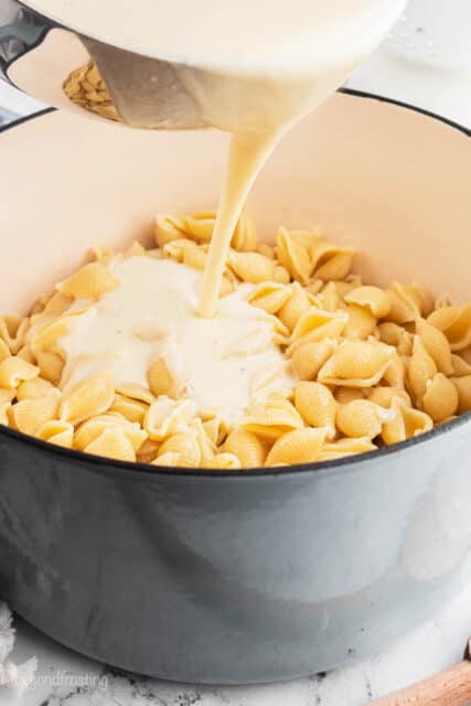 Cheese sauce being poured over pasta shells