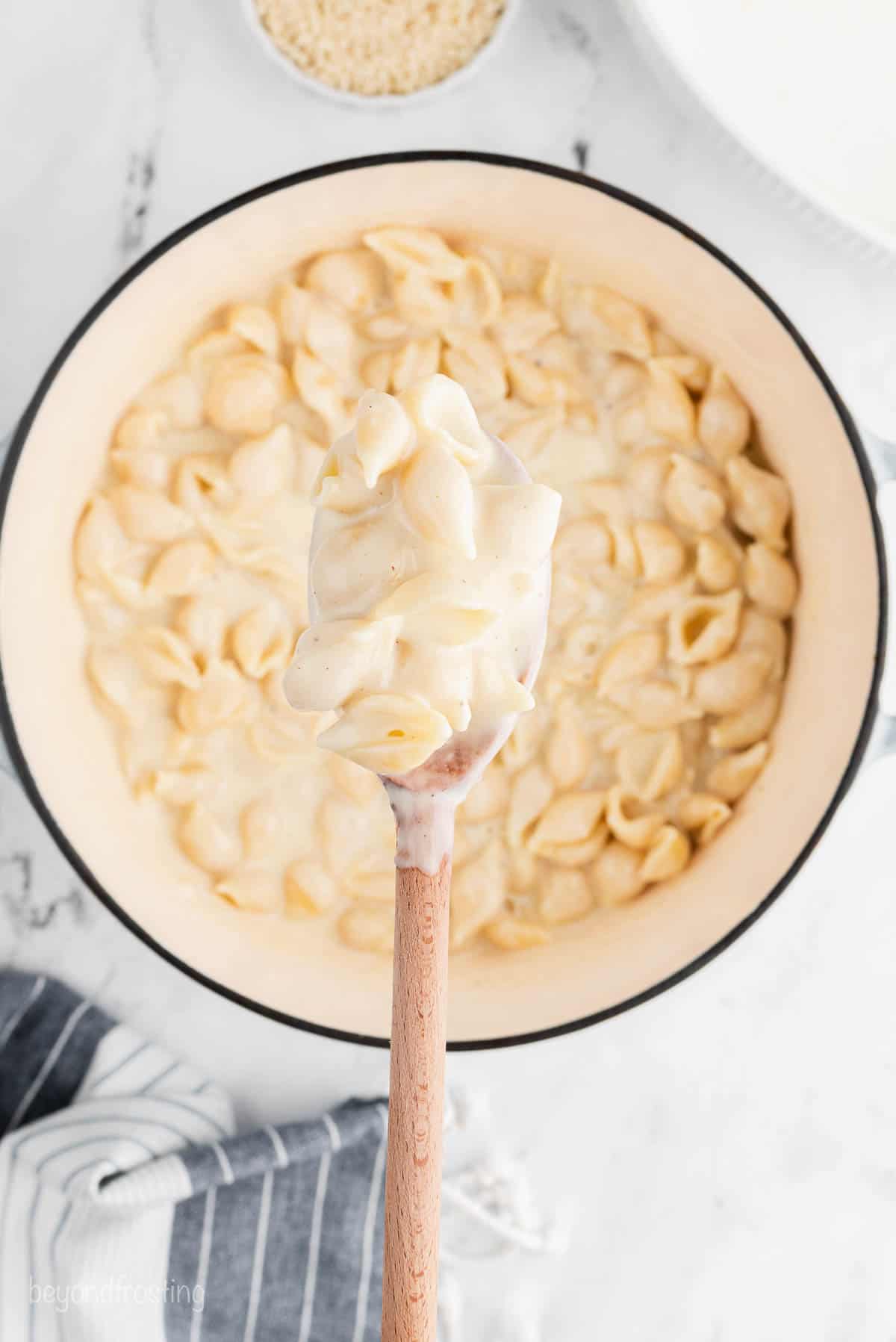 A wooden spoon mixing cheese sauce and pasta shells