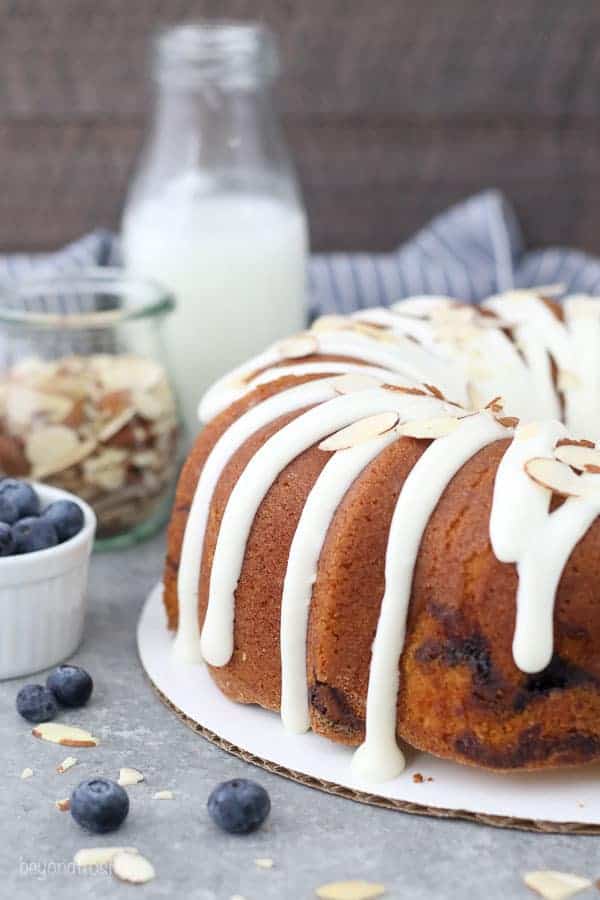 A bundt cake with a drippy cream cheese glaze and topped with shredded almonds